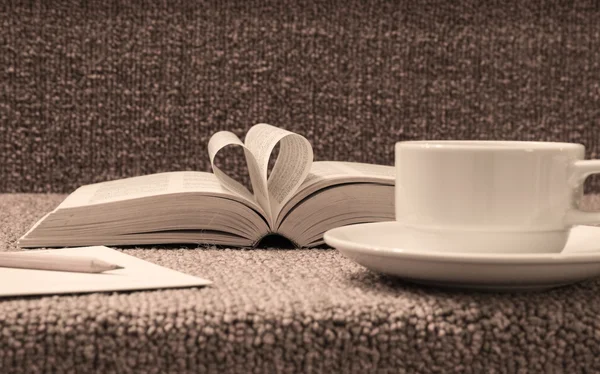 Pages of open book rolled in heart shape with coffee on table