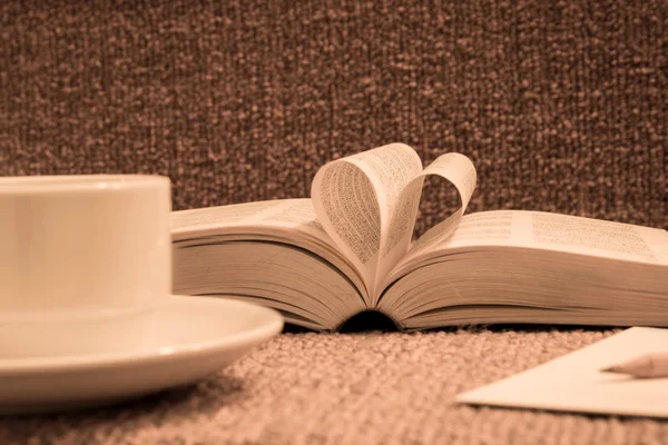 Pages of open book rolled in heart shape with coffee on table