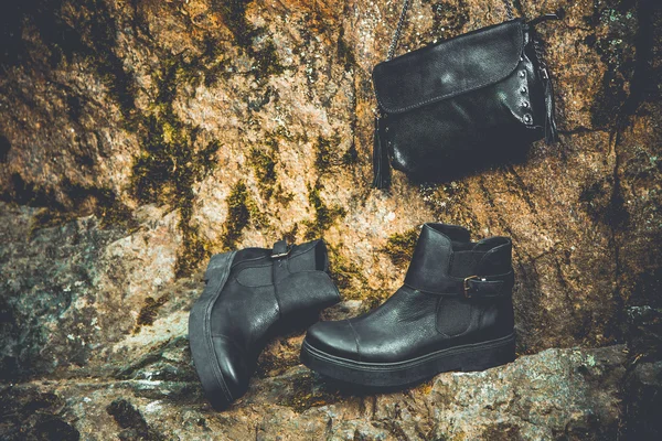 Black leather boots and black handbag on granite and moss, female soda