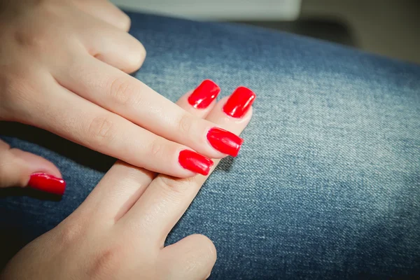 Red manicure, manicured hands, jeans background