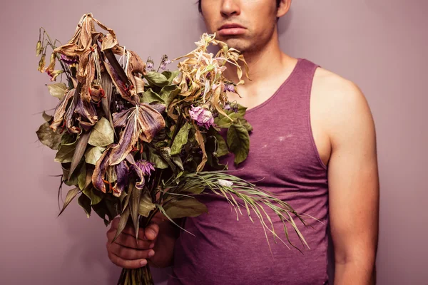 Young man holding bouquet of dead flowers