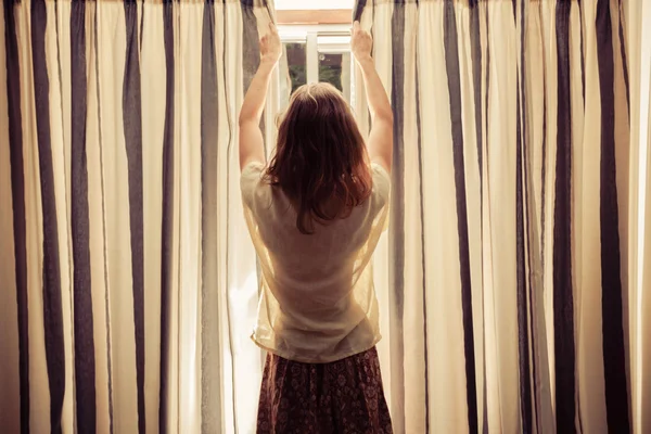 Young woman opening the curtains at sunrise
