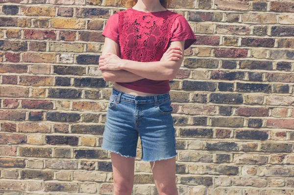 Young woman in red top standing by brick wall