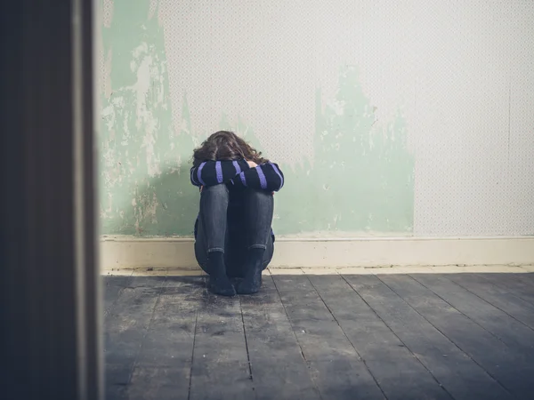 Sad young woman sitting on floor in empty room