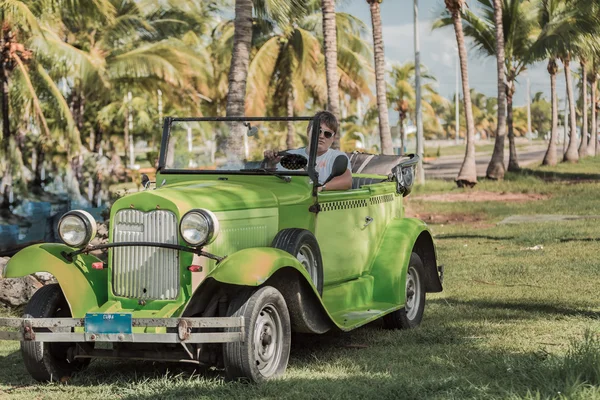 Green vintage  classic car with a young taxi driver at Cuban tropical garden