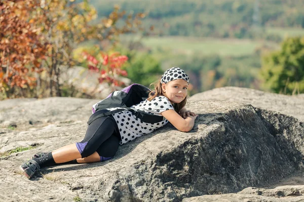 Happy, smiling little tired girl lying and resting on Niagara escarpment stone cliffs after hiking