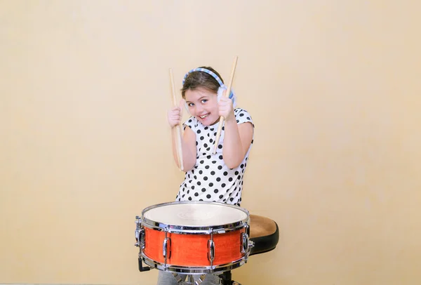 Joyful, charming fashionable little girl  in motion sitting behind the snare drum and holding a sticks in her hands