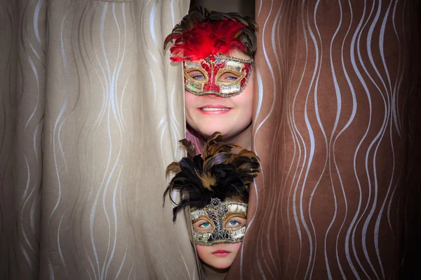 Closeup view of happy smile teenage boy and unhappy little girl in theatrical masks watching from behind a curtains