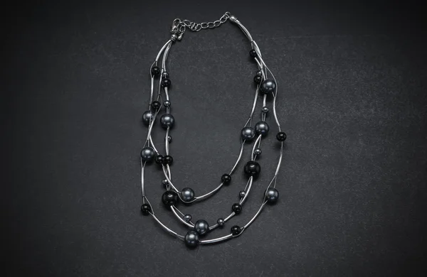 Great closeup view of styled  silver necklace with black and dark blue pearls isolated on dark