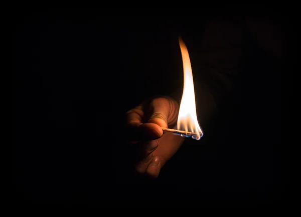Hand holding burning matchstick in darkness