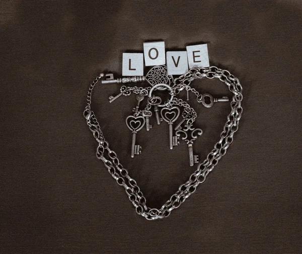 Silver chain shaped as valentine heart with various miniature keys in the middle and love ward above