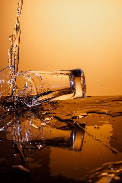 Exploding Glass cup with water shattering over orange background.