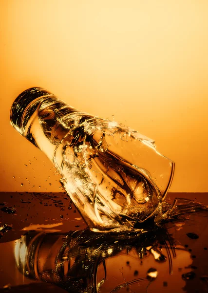Exploding Glass cup with water shattering over orange background.