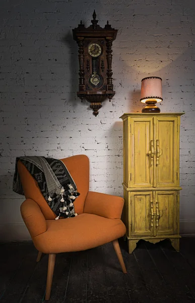 Orange armchair, yellow cupboard, pendulum clock and illuminated table lamp