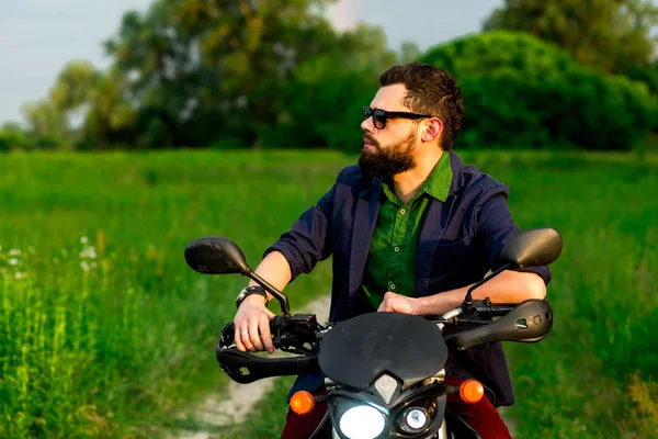 View of a man with a motorcycle on a dirt road among fields.