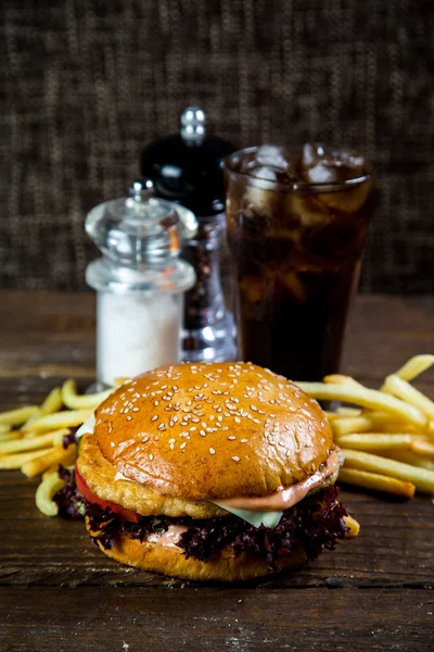 Big and tasty hamburger on desk with cola and fried potatoes on dark background