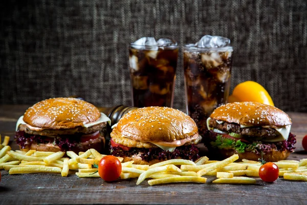 Big and tasty hamburger on desk with cola and fried potatoes on dark background