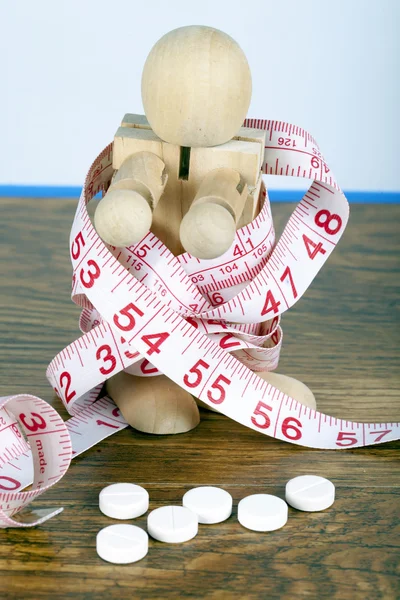 Weight loss concept with wooden man wrapped in measuring tape and diet pills