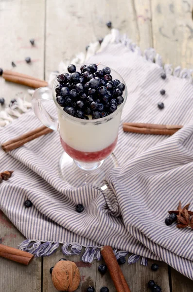 Delicious parfait dessert with bilberry, milk souffle and jello layers. Frozen treat in a glass on  rustic wooden background