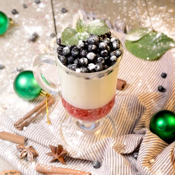 Delicious parfait dessert with bilberry, milk souffle and jello layers. Frozen treat in a glass on rustic wooden background