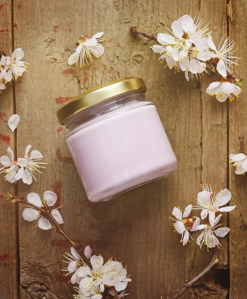 Organic cosmetic cream with apricot tree flowers on a wooden background. Vintage spa still life. Top view