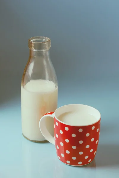 Vintage still life with red, in polka dot, cup of milk and antique bottle of milk on a blue background.