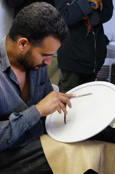 Ceramic artist makes a design on a plate in Fez, Morocco.