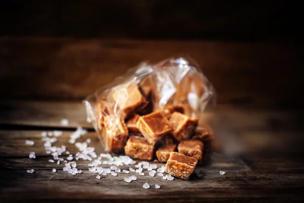 Heap of Salted caramel pieces and sea salt on a wooden table. Bu