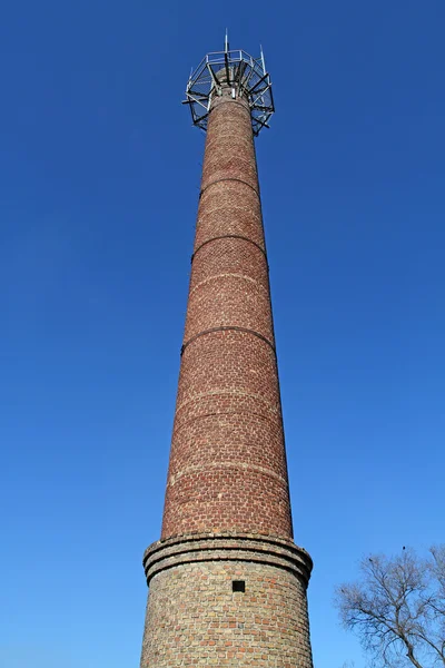 Old brick factory chimney high against the bright blue sky.