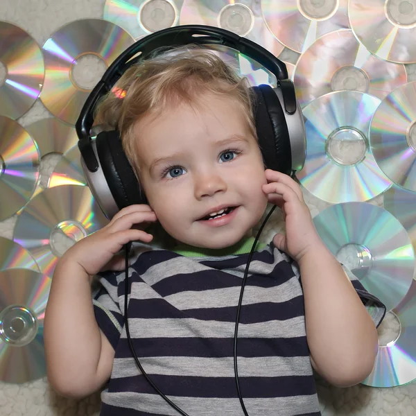 A little boy in headphones listens to music. White Boy in headphones lying on disks. Baby listening to a lullaby and is preparing to sleep