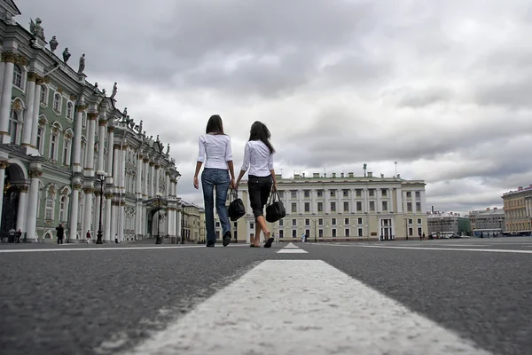 Two girls in the office are on the costumes of the old city of Europe. Business woman go on the roadway to the old buildings on the background of sky alarm