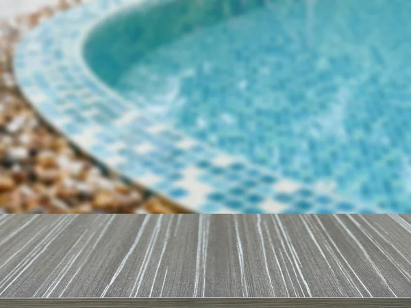 Empty wooden table with stone on the edge of the swimming pool b