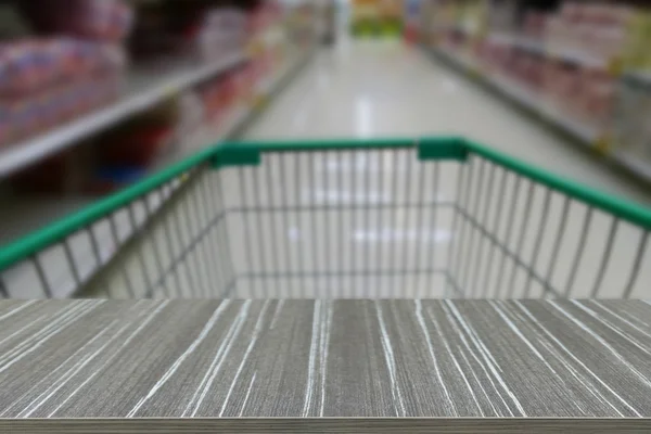 Empty wooden table with shopping cart in supermarket blur backgr