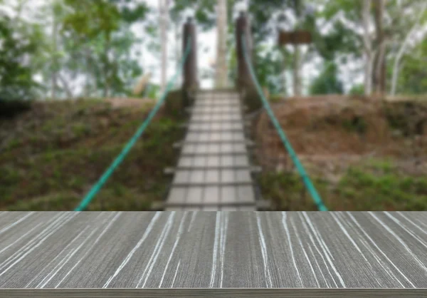 Empty wooden table with pedestrian rope bridge across valley blu