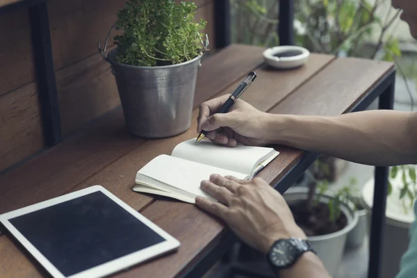 Man writing on notebook with digital tablet