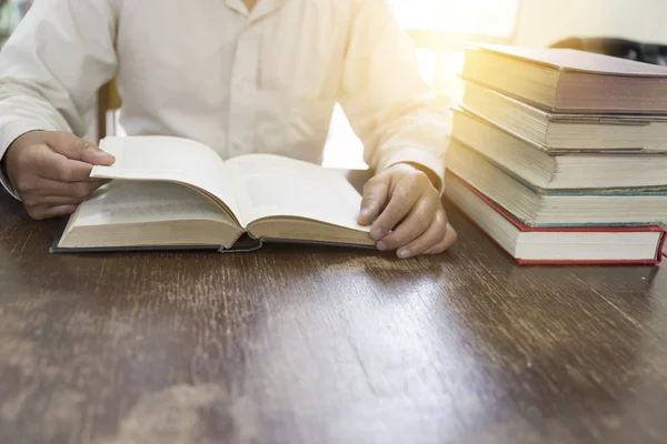 Man reading book with textbook stack on wooden desk