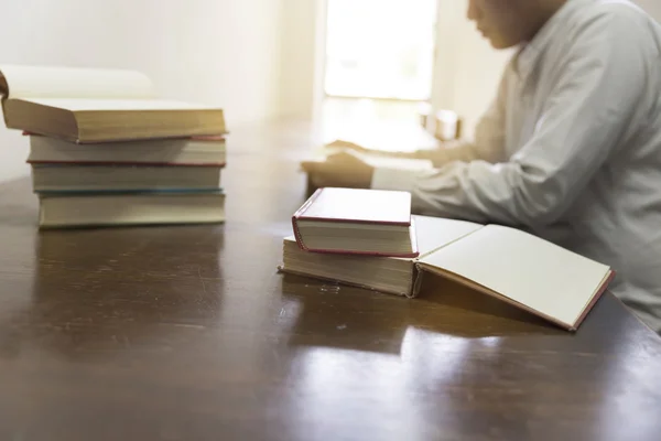 Man reading book with textbook stack on wooden desk