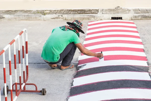Worker using brush for painting white line on the road