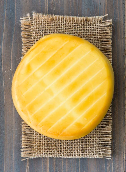 Smoked cheese wheel, tomatoes and bread on wooden table