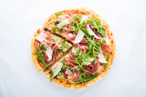 Sliced pizza with prosciutto (parma ham), arugula (salad rocket) and parmesan on white background top view. Italian cuisine.
