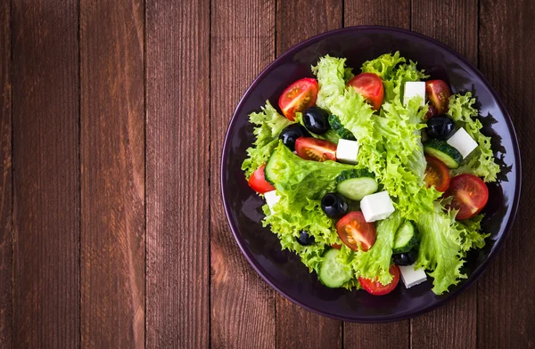 Greek salad (lettuce, tomatoes, feta cheese, cucumbers, black olives) on dark wooden background top view.