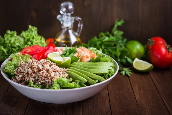 Healthy salad bowl with quinoa, tomatoes, chicken, avocado, lime and mixed greens (lettuce, parsley) on wooden background close up.