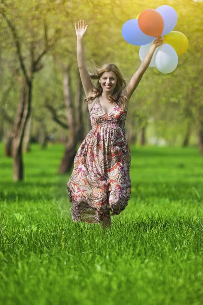 Modern Lifestyle Concept. Young Caucasian Blond Female with Bunch of Colorful Air Balloons Running in Spring Forest