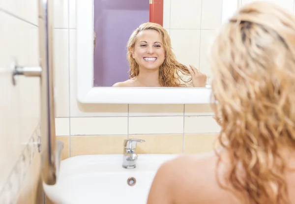Happy Caucasian Woman Looking At Mirror\'s Reflection and Examining Her Face and Hair.