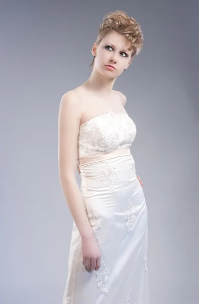 Fashion Concepts. Young Sexy Blond Woman in Nicely Tailored Wedding Dress Posing Against Gray