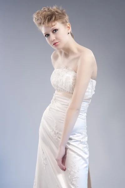 Fashion Concepts. Tall Young and Sexy Blond Woman in Tailored Wedding Dress Posing Against Gray