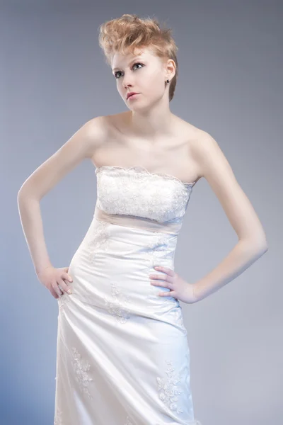 Fashion Concepts. Tall Young and Sexy Blond Woman in Tailored Wedding Dress Posing Against Gray