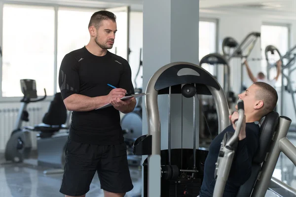 Personal Trainer Takes Notes While Man Exercising Chest