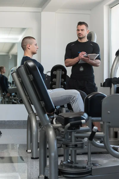 Personal Trainer Takes Notes While Man Exercising Legs