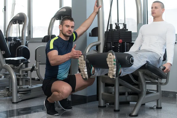 Man Train Legs On Machine With Personal Trainer